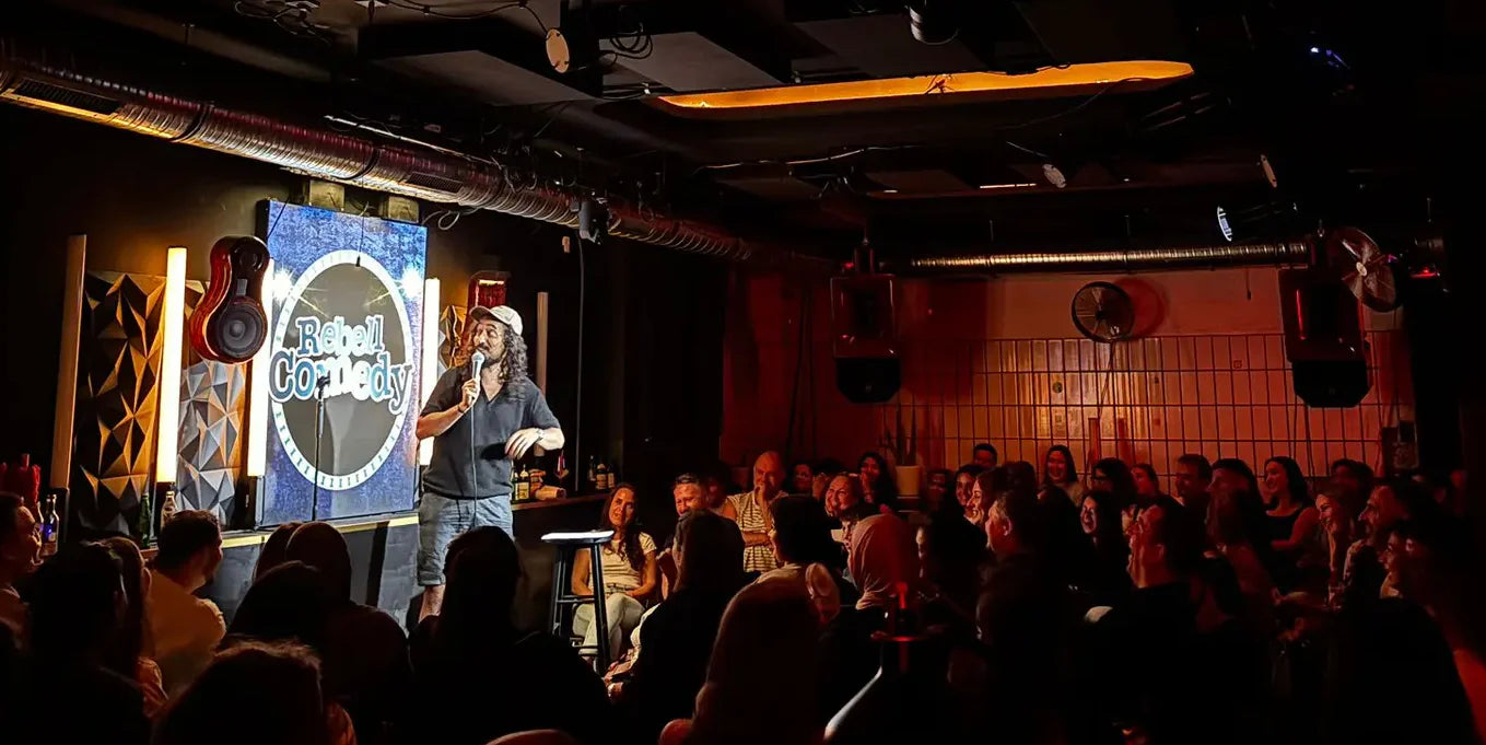 Person on stage with a microphone in a dimly lit room with people seated.